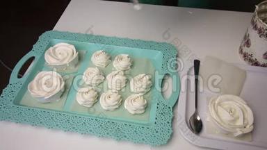 托盘上摆着一个玫瑰形的棉花糖。 一个女人用一个糕点包在旁边形成各种形状的棉花糖。